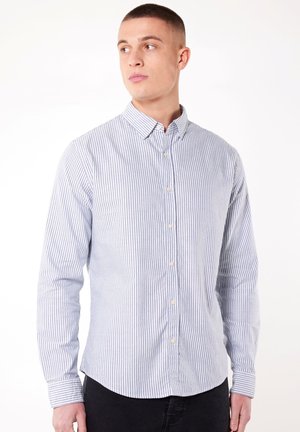 Camisa de rayas azul y blanca de manga larga con cuello abotonado, que presenta pequeños botones y un dobladillo curvado. Fabricada en un tejido ligero.