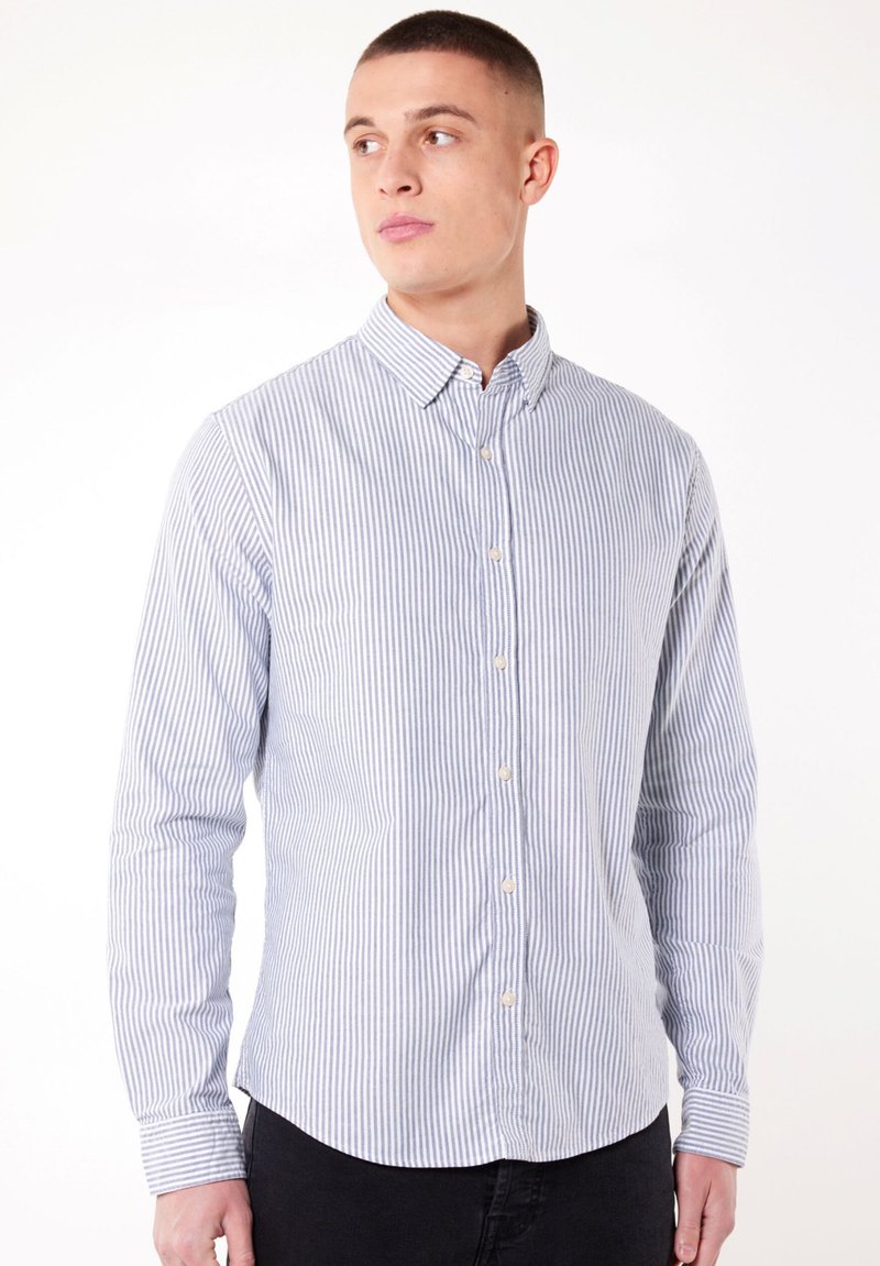 Chemise à manches longues rayée bleu et blanche avec un col à bouton, dotée de petits boutons et d'un ourlet arrondi. Fabriquée en tissu léger.