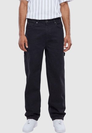 Pantalones de mezclilla negros con un corte relajado, que presentan un diseño clásico de cinco bolsillos y una textura ligeramente desvaída, combinados con zapatillas blancas.