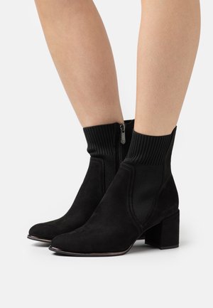 Bottines en daim noir avec une tige en tissu côtelé, fermeture éclair latérale et talon bloc. Présente une surface lisse et des accents de couture minimalistes.