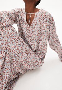 Robe longue à manches longues avec un col en V et une fermeture à nouer. Présente un mélange de fleurs rouges, bleues et blanches sur un fond clair. Tissu doux et fluide.