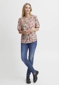 Kwiatowa bluzka z krótkimi puff sleeves w kolorze różowym, zielonym i żółtym na jasnym tle; połączona z niebieskimi dżinsami i czarnymi butami.