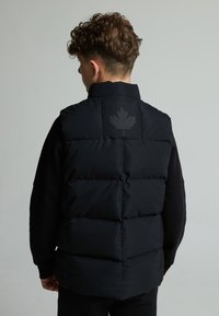 Chaleco acolchado negro con un cuello alto, que presenta un diseño de hoja de arce reflectante con puntos en la parte posterior y una tela suave y texturizada.