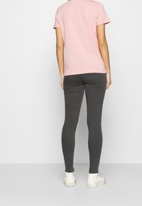 Rosa bomullströja med korta ärmar, kombinerad med mörkgrå leggings. Outfiten kompletteras med vita, låga sneakers.