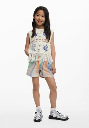 Gehaakte top met franjes, met geborduurde blauwe ontwerpen; tie-dye shorts in pastelkleuren; metallic sandalen met bandjes; gelaagde sokken.