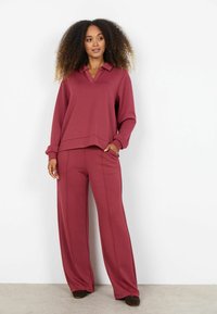 Bordeauxkleurige set bestaande uit een top met lange mouwen en kraag, gecombineerd met een broek met wijde pijpen. Zacht van textuur, comfortabele pasvorm, met steekzakken aan de zijkant van de broek.