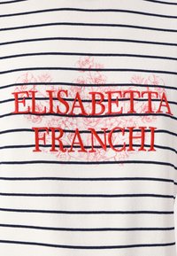 Top a rayas blancas y marinas con texto bordado en rojo "ELISABETTA FRANCHI" y un diseño floral en el fondo. Textura de tela suave.