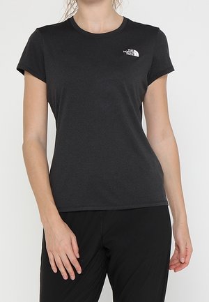 Kobieta nosząca dopasowaną czarną koszulkę z krótkim rękawem z małym białym logo The North Face po lewej stronie klatki piersiowej.