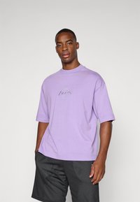 Purple cotton t-shirt with short sleeves, featuring an embroidered "Lakers" logo on the chest. Worn with black mesh shorts.