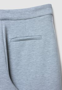Pantalon de survêtement gris clair avec une texture lisse, une ceinture élastique et une poche latérale intégrée avec des coutures soignées.