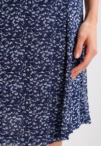 Navy blue dress featuring a floral pattern in light blue and lavender. Made from lightweight fabric with a flowy design and subtle texture.