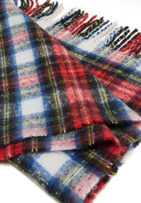 Écharpe tartan en laine douce, pliée, présentant un motif à carreaux rouge, bleu, noir, blanc et jaune avec des bords frangés sur un fond blanc.