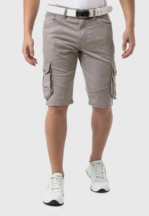 Shorts cargo rayés beiges avec deux poches latérales et une ceinture blanche. Portés avec des chaussures de sport blanches. Présentent une coupe décontractée et un design jusqu'aux genoux.