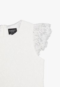 Vit klänning med en blommig spetsöverdrag, korta spetsärmar, rund halsringning och en dold dragkedja på ryggen. Mjuk, texturerad tyg.