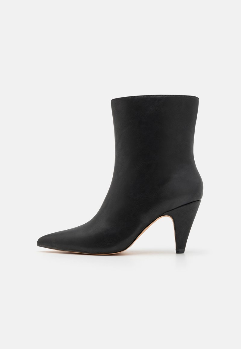 Bottine en cuir noir avec un bout pointu et un talon sculpté. La tige présente une texture lisse et une coupe ajustée.