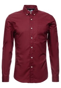 Pánská dlouhá burgundská košile na knoflíky s přední kapsou a límečkem na knoflíky, vystavená na bílém pozadí.