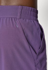 Shorts de sport violets en tissu léger et texturé. Équipés d'une taille élastique et de poches latérales pour plus de praticité.