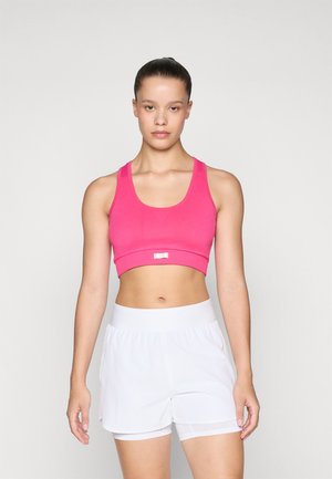 Rosa cropped sports-bh med brede stropper og en liten metallaccent. Kombinert med hvite treningsshorts med elastisk midjebånd.