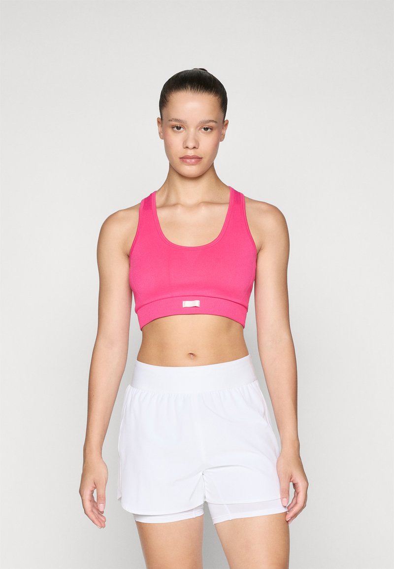 Rosa cropped sports-bh med brede stropper og en liten metallaccent. Kombinert med hvite treningsshorts med elastisk midjebånd.