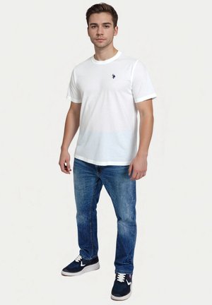 T-shirt en coton blanc avec un col rond et des manches courtes, orné d'un petit logo bleu marine. Assorti à un jean en denim et des baskets bleu marine.
