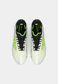 Valkoiset ja neonvihreät urheilukengät mustilla nauhoilla, mustalla sisustalla ja suurella vihreällä "N"-logolla, nähtynä ylhäältä päin valkoista taustaa vasten.