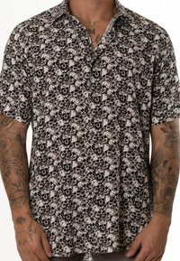Camisa de manga corta con estampado de calaveras en blanco y negro sobre un fondo claro, confeccionada en una tela ligera con cuello y botones.