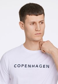 Weißes Baumwoll-T-Shirt mit "KOPENHAGEN" und "LINDBERGH" in Dunkelblau bedruckt. Mit rundem Halsausschnitt und kurzen Ärmeln. Angenehme Textur.