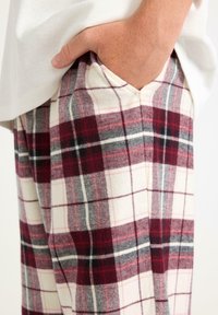 Spodnie flanelowe w kratkę w kolorach burgundowym, białym i szarym, o luźnym kroju z bocznymi kieszeniami. Miękka faktura, casualowy design.