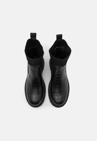 Botines negros con un patrón de cocodrilo, cuello de punto acanalado y tira de agarre. Textura suave con puntera redondeada y suela de goma.