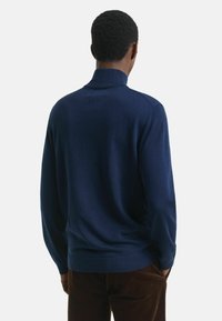 Marineblauwe pullover trui met een hoge kraag, lange mouwen en een gladde textuur; heeft een getailleerd silhouet en een ribbelrand.