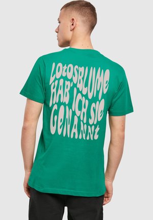 Grünes Baumwoll-T-Shirt mit lockerer Passform, das auf der Rückseite großen, weißen, gewellten Text zeigt mit der Aufschrift "Lotosblume hab’ ich sie genannt."