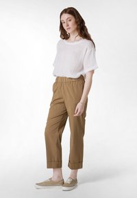 Biała lniana bluzka z krótkim rękawem i okrągłym dekoltem, zestawiona z beżowymi spodniami o elastycznym pasie w kroju zwężanym oraz jasnobrązowymi butami na sznurówki.