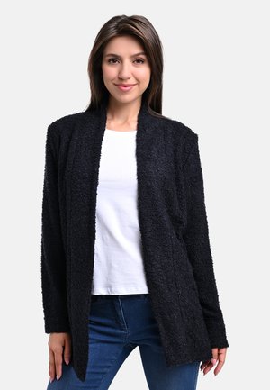 Schwarze, strukturierte Strickjacke mit offenem Frontdesign, langen Ärmeln und lässiger Passform. Getragen über einem weißen Hemd und blauen Jeans.