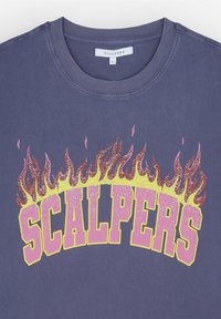 Camiseta azul oscuro con cuello redondo; presenta un gran logo de "SCALPERS" brillante en amarillo y rosa, acentuado por gráficos de llamas sobre el texto.