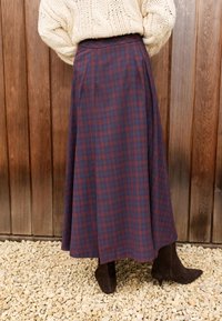 Dolga krilo s karo vzorcem v mornarsko modri in bordo barvi, z zračnim dizajnom in visokim pasom. Oblečeno s parom rjavih antilop gležnjarjev.