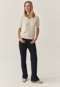 Jersey de manga corta acanalado en color crema con escote en forma de V, combinado con unos jeans de campana de color azul oscuro. Los jeans tienen una sutil abertura en el dobladillo.