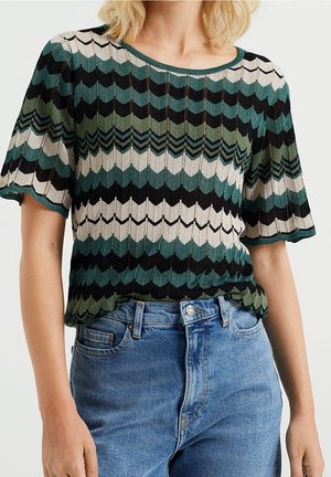 Krótki top z krótkim rękawem w zygzakowaty wzór w kolorach zielonym, czarnym i beżowym, wykonany z dzianiny o fakturze. Połączony z wysokim stanem niebieskich jeansów.