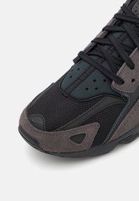 Svart och grå sneaker med en kombination av mesh och mocka, med en texturerad gummisula och snörning framtill.