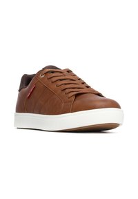 Baskets en cuir marron avec une semelle en caoutchouc blanche, présentant un bout rond, des accents texturés et un col en tissu marron. Les lacets sont également marron.