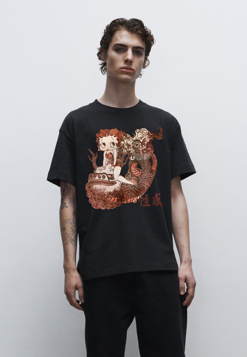 Černé tričko s detailním grafikou postavy a draka v červených a oranžových odstínech. Krátké rukávy a volný střih.