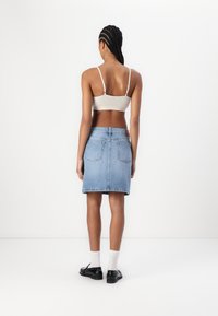 Svetlo bež prilegajoči bralette in mid dolga denim krila s ravnim rezom v svetlo modri barvi, ki ima zadnje žepe in usnjeno oznako.