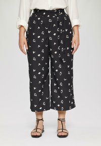 Zwarte culottebroek met een wit abstract patroon, voorzien van een elastische tailleband en strik. Zachte, gestructureerde stof, cropped lengte. Zwarte sandalen zichtbaar.