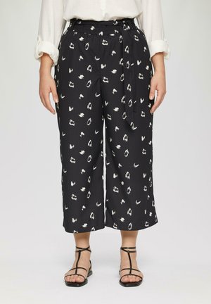 Zwarte culottebroek met een wit abstract patroon, voorzien van een elastische tailleband en strik. Zachte, gestructureerde stof, cropped lengte. Zwarte sandalen zichtbaar.