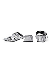 Zilveren hoge hakken sandalen met kruislingse banden voorzien van ronde studs, textuur oppervlak en een lage blokhak. Zwart accent op de zool.
