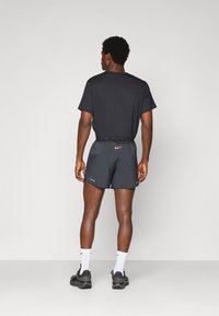 Männliches Sportoutfit mit einem schwarzen Kurzarmshirt und schwarzen Laufshorts mit reflektierenden Akzenten sowie Nike-Branding am Bund.