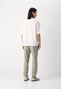 White short-sleeve shirt with subtle texture, green linen pants, and beige sneakers with brown stripes, viewed from the back.