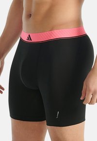 Svarta sportshorts med en rosa elastisk midja med ribbad textur och Adidas-logotyp. Slät tyg, figurnära design, midjehöjd.