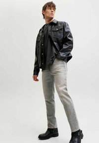 Chaqueta de cuero negra con dos bolsillos frontales, sobre una camiseta oscura. Jeans gris claro, de corte ajustado, y botines negros completan el conjunto.