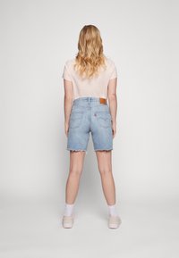 Light pink T-shirt and high-waisted denim shorts, featuring a frayed hem and a tan leather patch on the back waist. Casual footwear and socks visible.