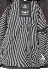 Veste d'extérieur noire avec un intérieur rayé verticalement en blanc, comportant une étiquette, une poche et une petite ouverture pour appareil avec une bordure accentuée.